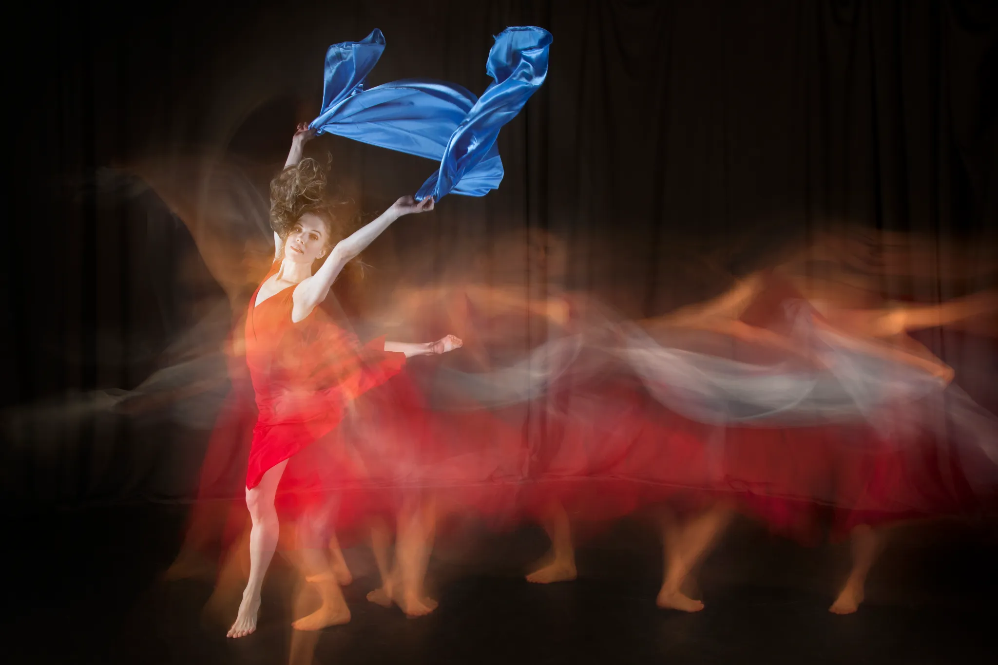 Long-exposure photograph of a dancer in red lifting blue fabric